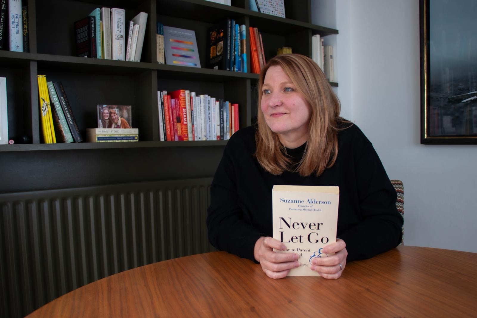 Suzanne Alderson at a table, holding a copy of her book Never Let Go.