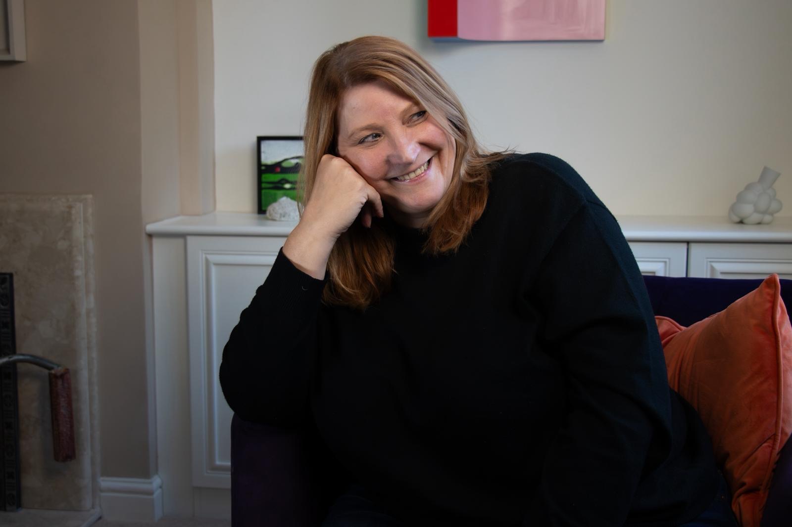 Suzanne Alderson sitting on a sofa, her head resting on her hand, smiling.